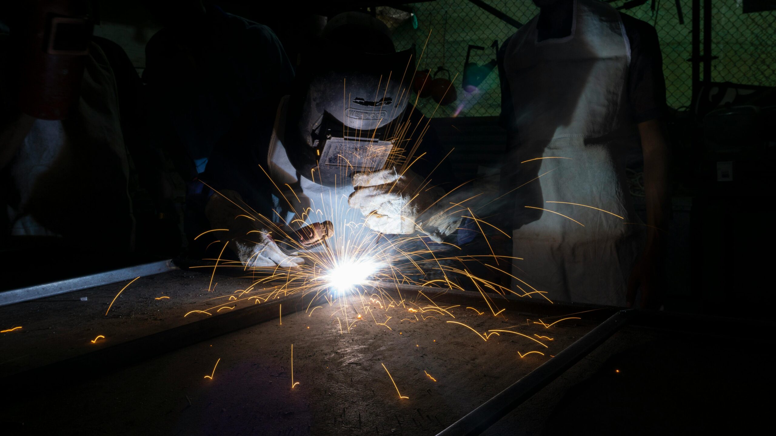 Skilled welder in protective gear creating sparks in a dark workshop environment.
